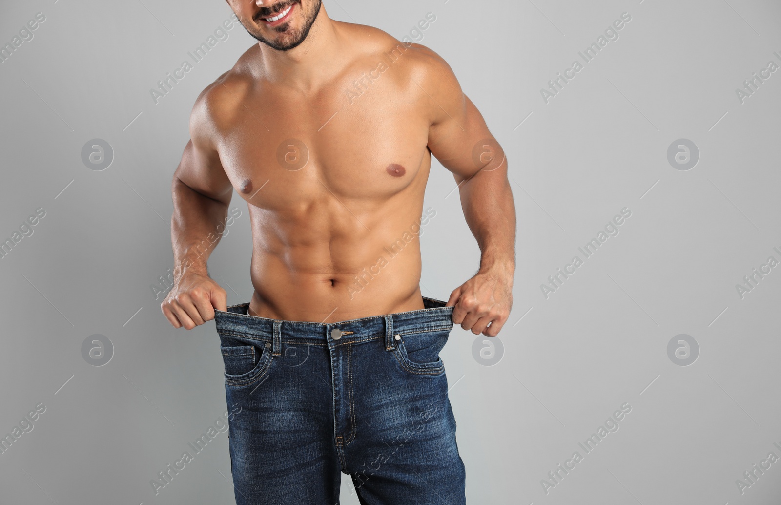 Photo of Young man with slim body in old big size jeans on grey background, closeup view