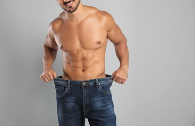 Young man with slim body in old big size jeans on grey background, closeup view