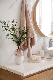 Photo of Vase with beautiful branches and toiletries on countertop in bathroom. Interior design