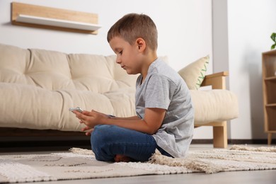 Photo of Boy with poor posture using phone on beige carpet in living room. Symptom of scoliosis