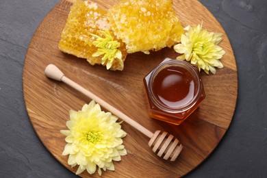 Photo of Sweet honey in jar, dipper, chrysanthemum flowers and pieces of honeycomb on grey textured table, top view
