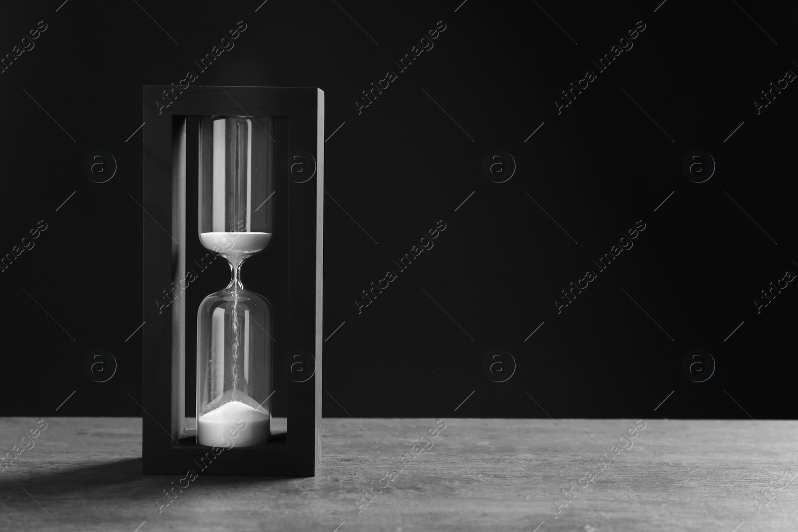 Photo of Hourglass with flowing sand on table against black background. Time management