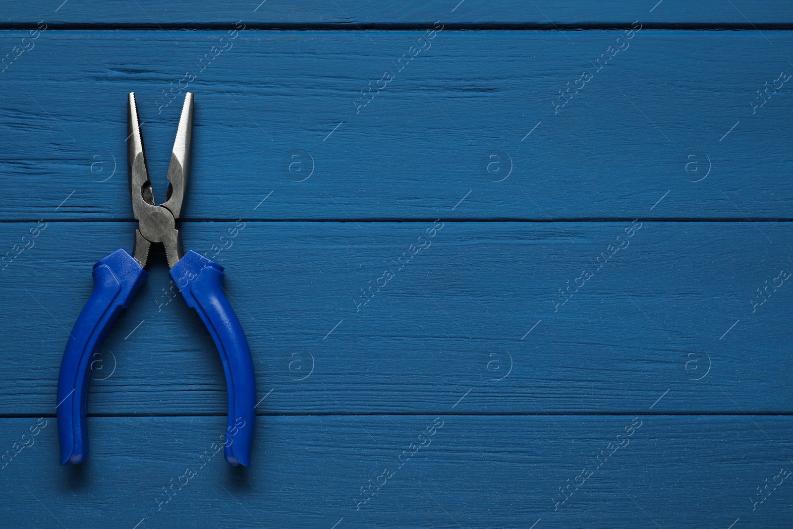 Photo of Needle nose pliers on blue wooden table, top view. Space for text