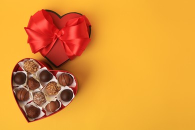 Photo of Heart shaped box with delicious chocolate candies on yellow background, flat lay. Space for text