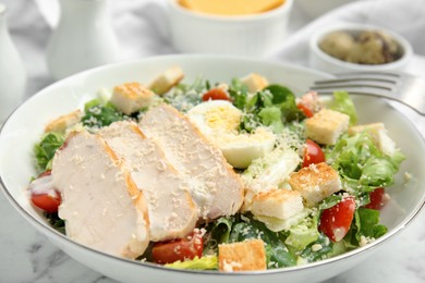 Photo of Delicious Caesar salad in bowl on white marble table, closeup