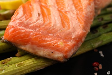 Tasty grilled salmon with asparagus and spices on plate, closeup