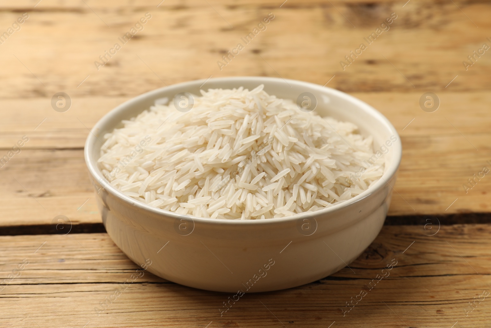 Photo of Raw basmati rice in bowl on wooden table, closeup