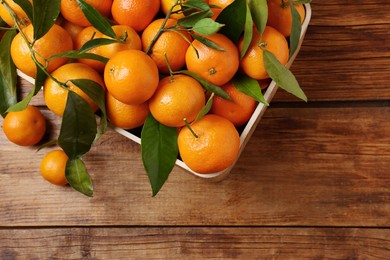 Photo of Fresh tangerines with green leaves in crate on wooden table, top view. Space for text
