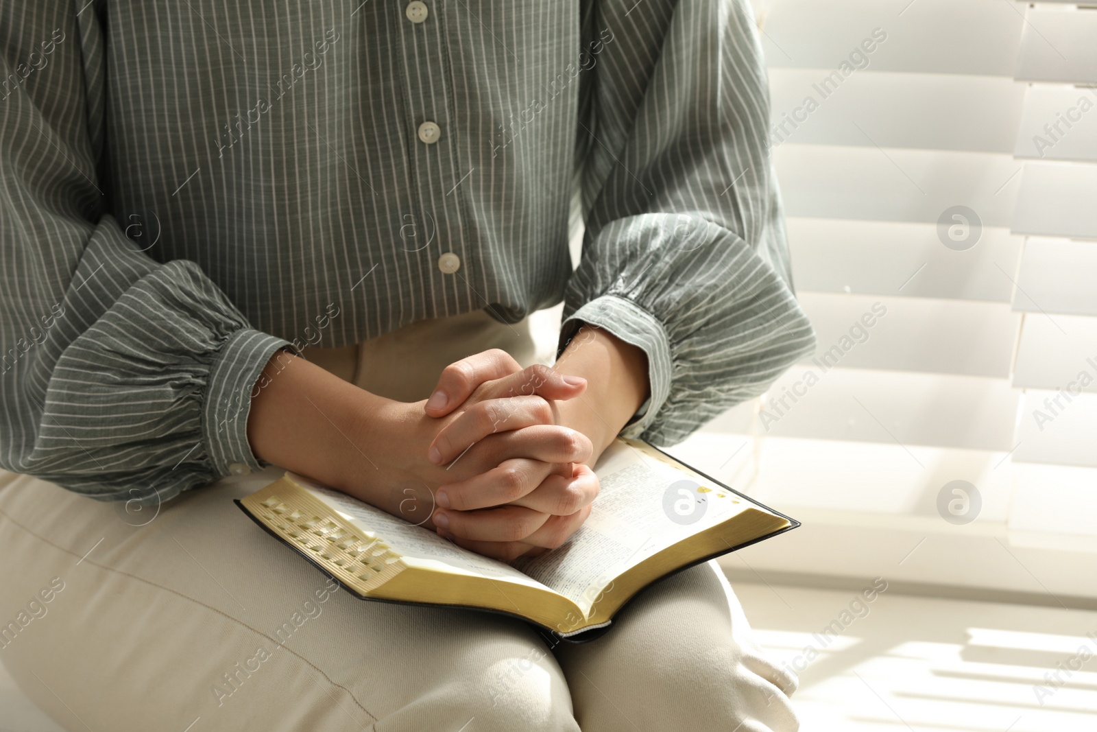 Photo of Religious woman praying over Bible near window indoors, closeup