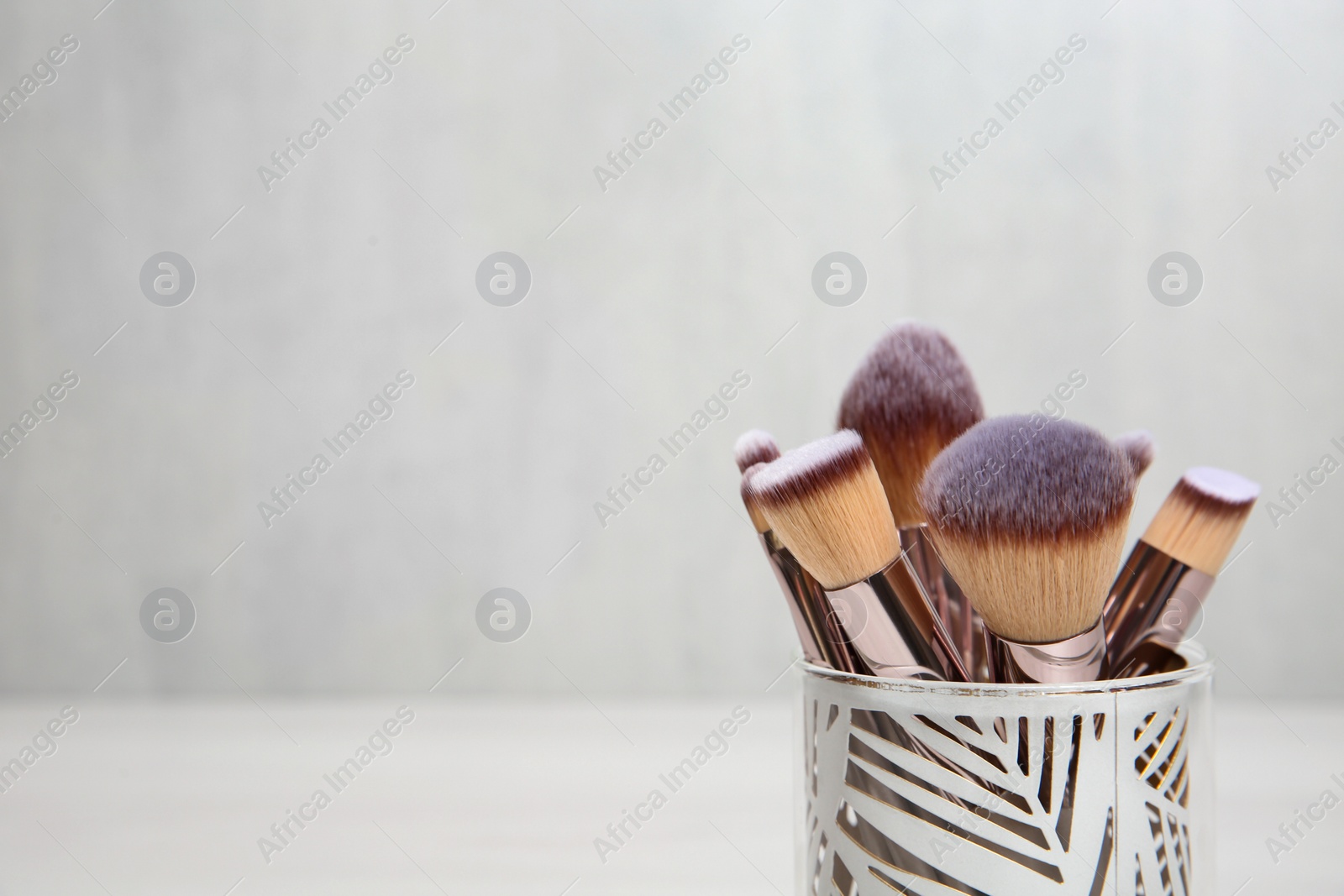 Photo of Organizer with professional makeup brushes against light background. Space for text