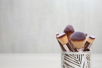 Photo of Organizer with professional makeup brushes against light background. Space for text