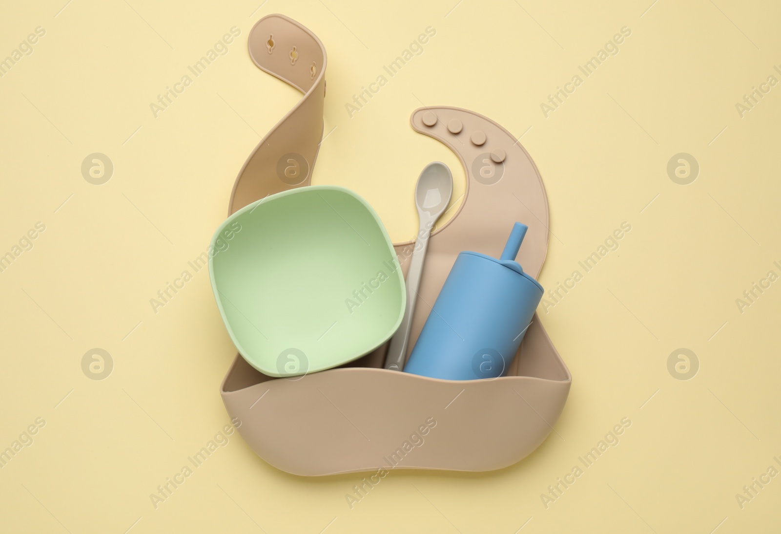 Photo of Baby feeding accessories and bib on yellow background, top view