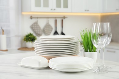 Photo of Clean plates, glasses, butter dish and floral decor on white marble table in kitchen