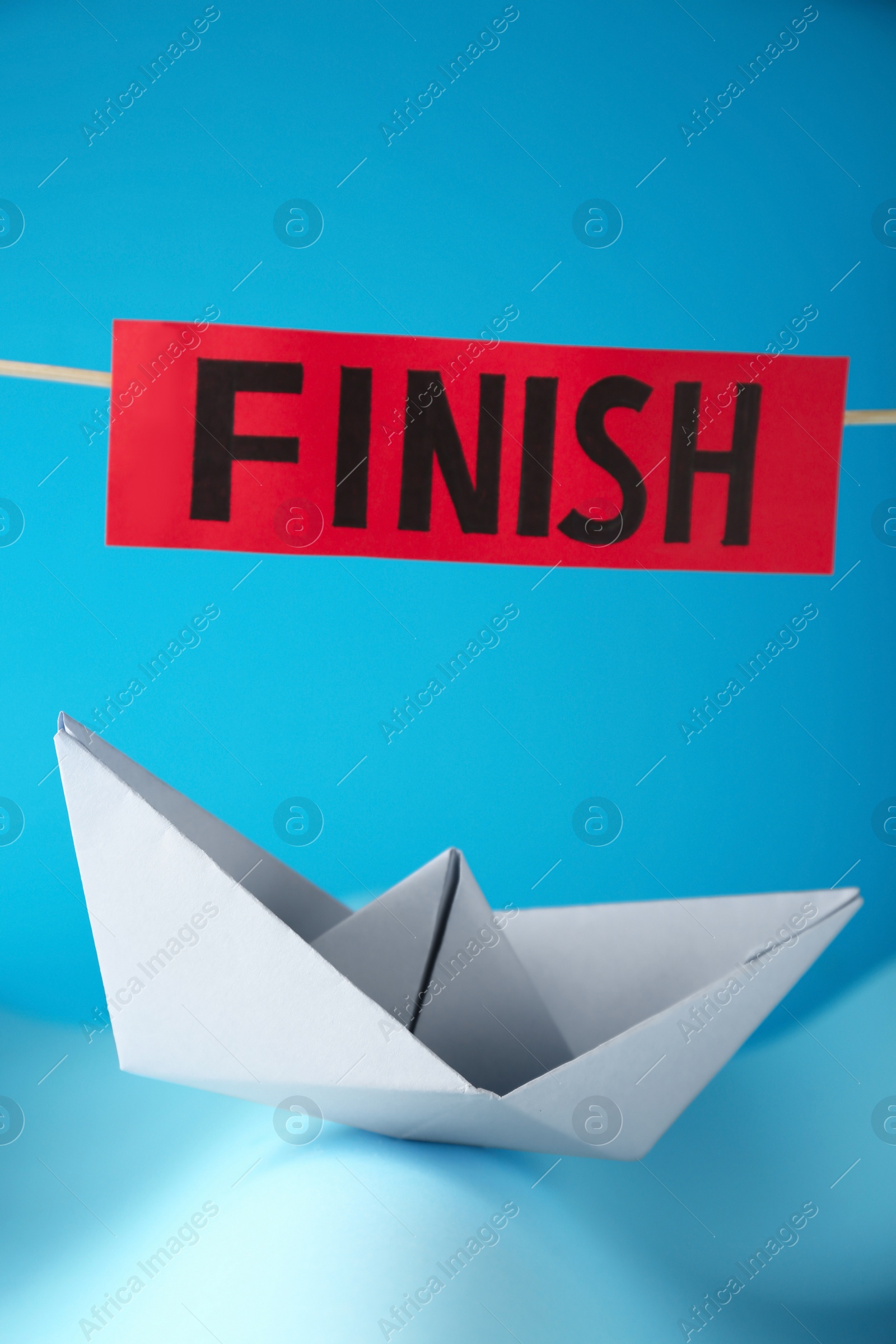 Photo of Competition concept. Paper boat among waves and red sign with word Finish on light blue background