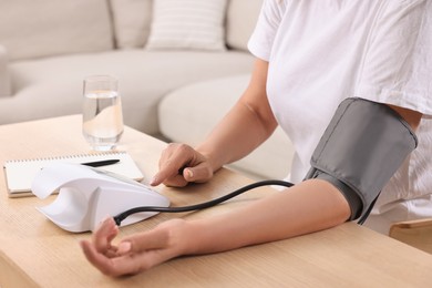 Photo of Woman measuring blood pressure at wooden table indoors, closeup