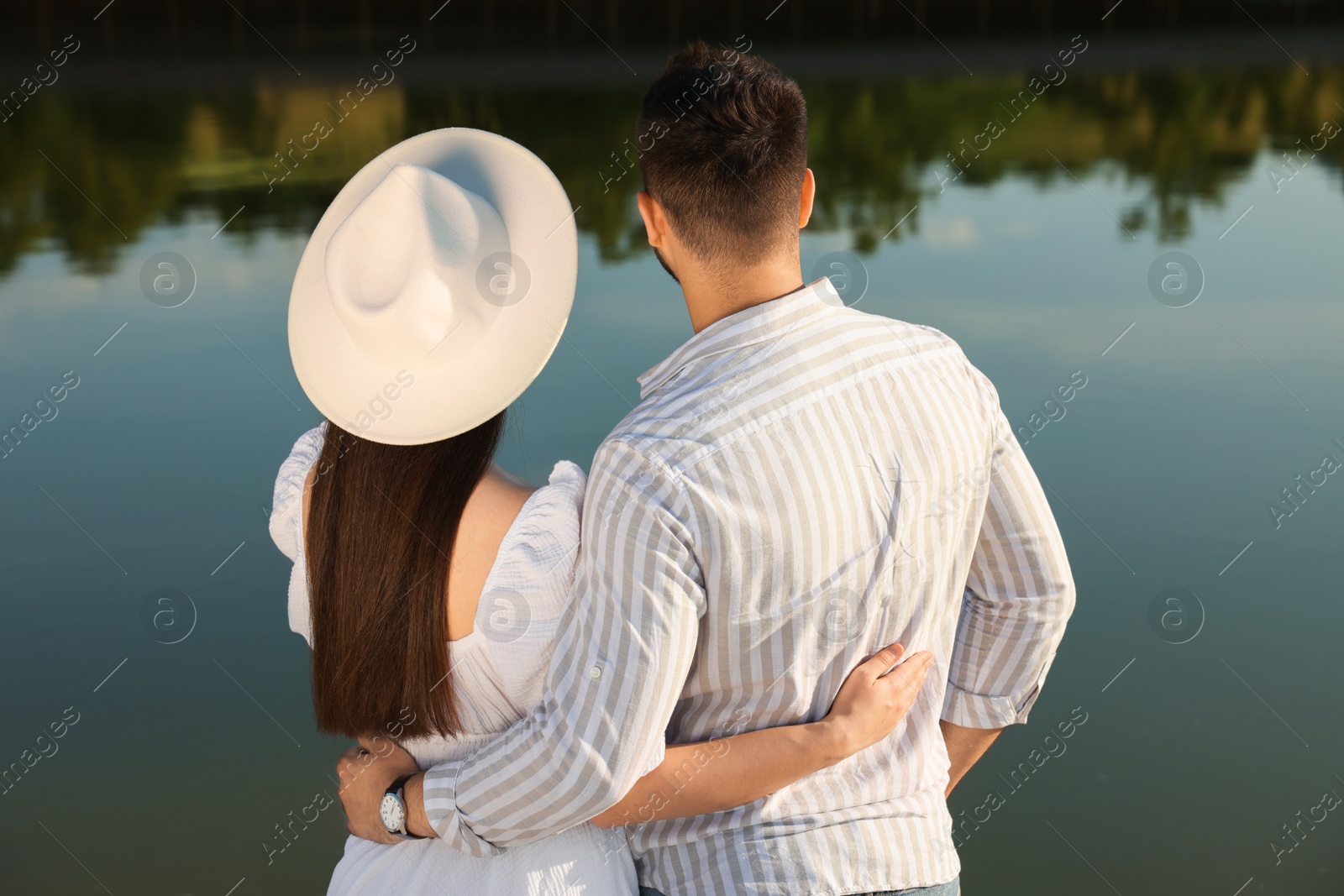 Photo of Romantic date. Couple spending time together near lake, back view