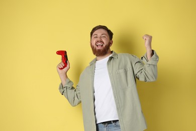 Happy man with game controller on pale yellow background