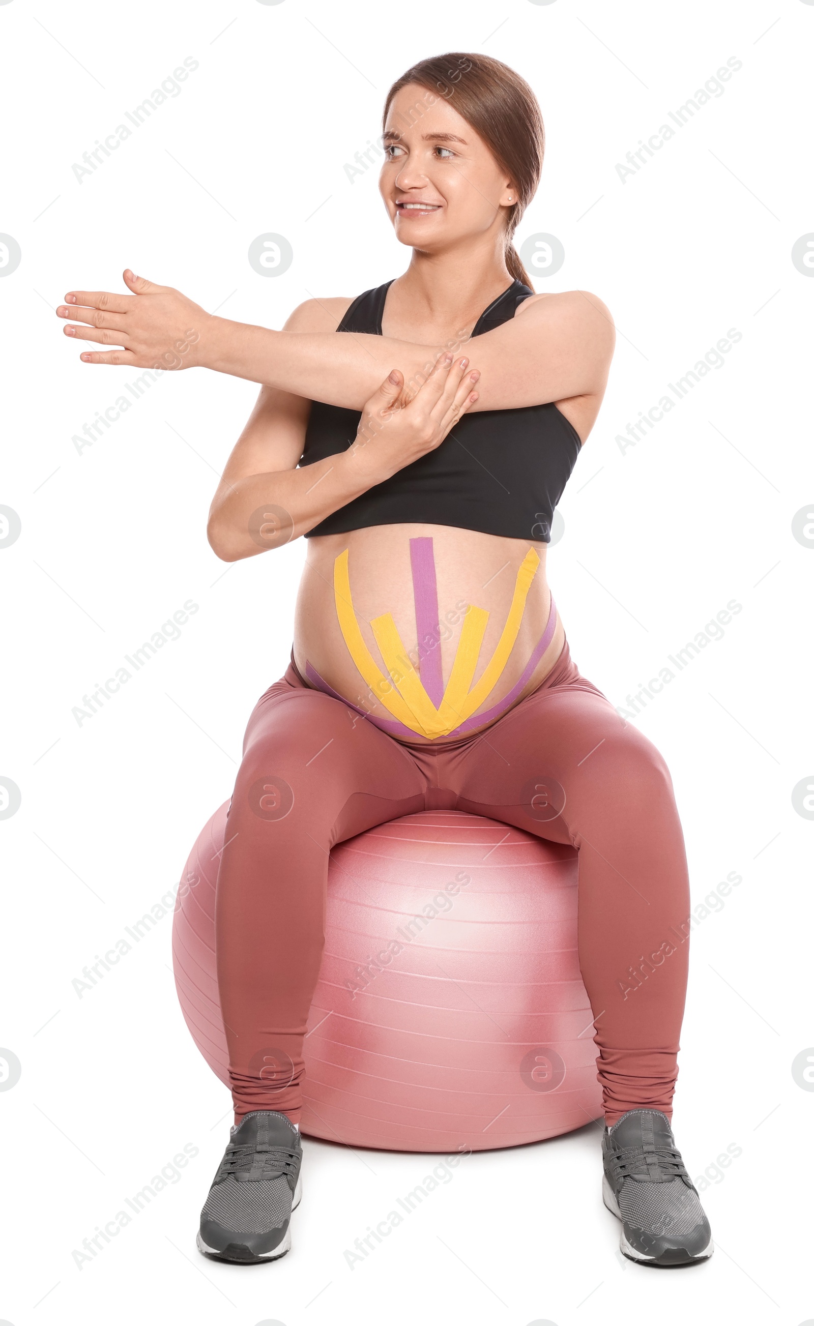 Photo of Sporty pregnant woman with kinesio tapes doing exercises on fitball against white background