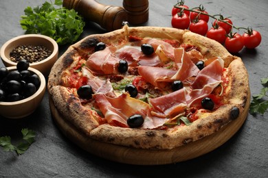 Tasty pizza with cured ham, olives, tomatoes, parsley and spices on black table