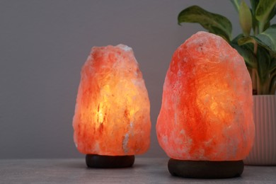 Photo of Himalayan salt lamps and houseplant on stone table near light grey wall