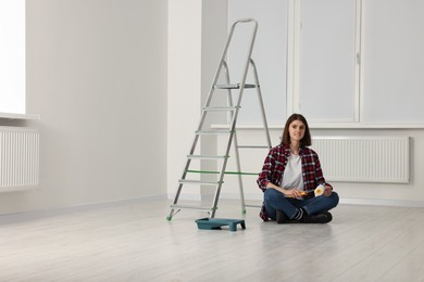 Young woman with roller sitting near stepladder indoors. Room renovation