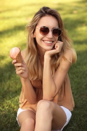 Happy young woman with delicious ice cream in waffle cone outdoors