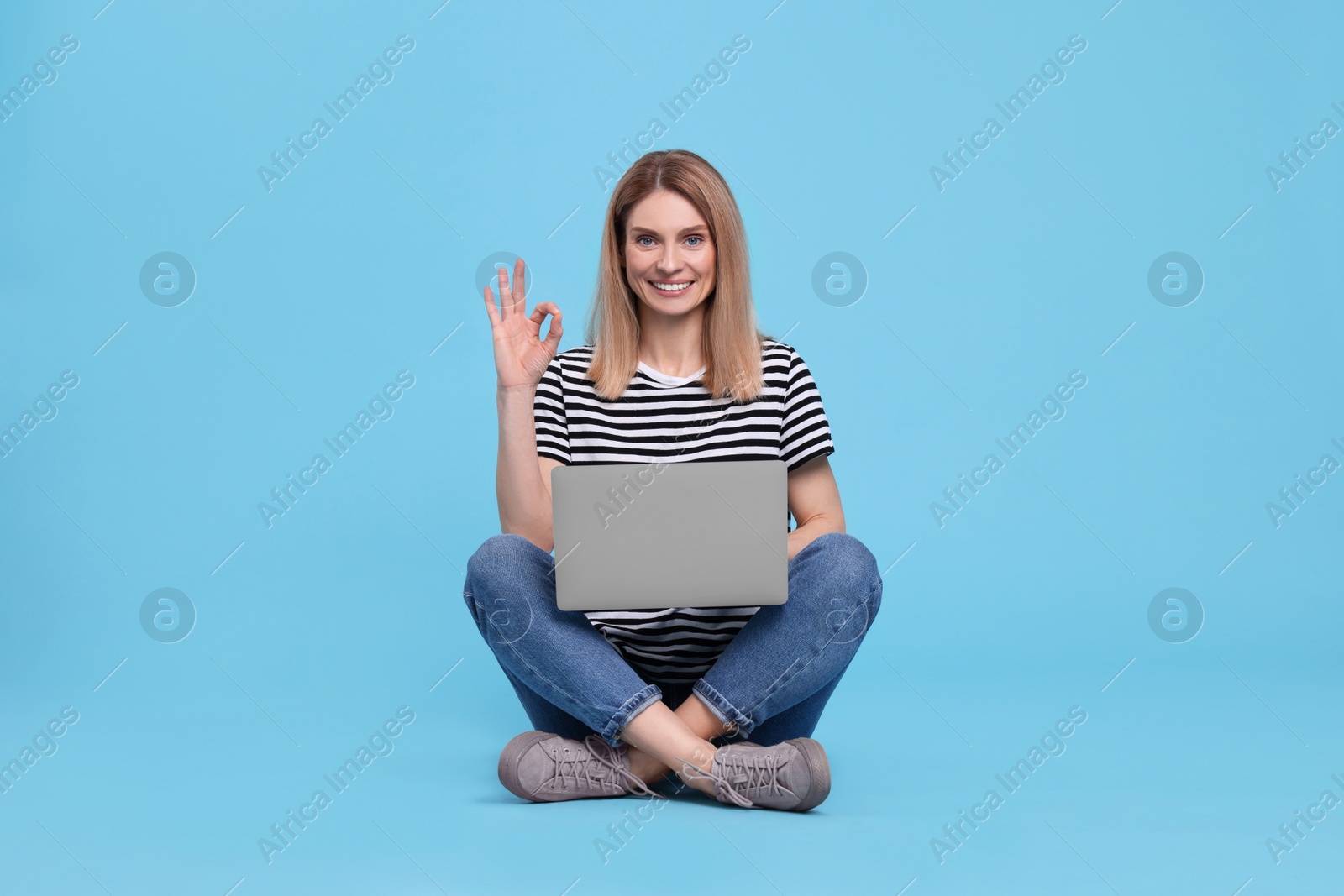 Photo of Happy woman with laptop showing ok gesture on light blue background