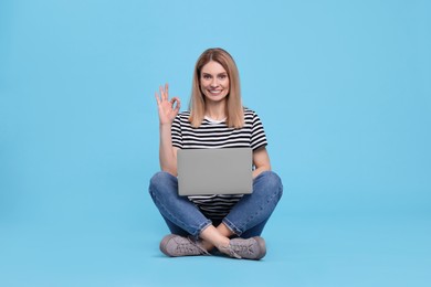 Happy woman with laptop showing ok gesture on light blue background
