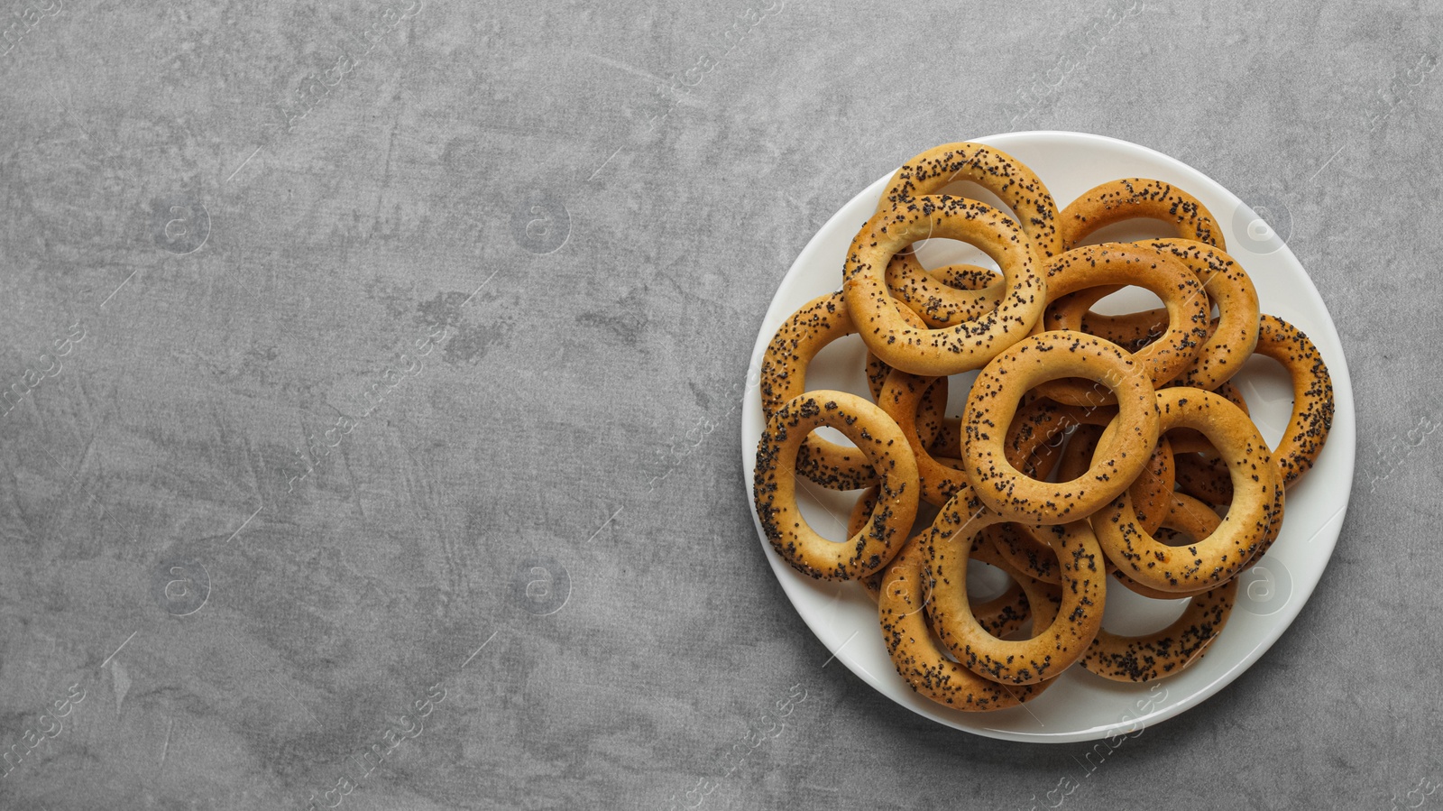 Photo of Plate with delicious ring shaped Sushki (dry bagels) on light grey table, top view. Space for text