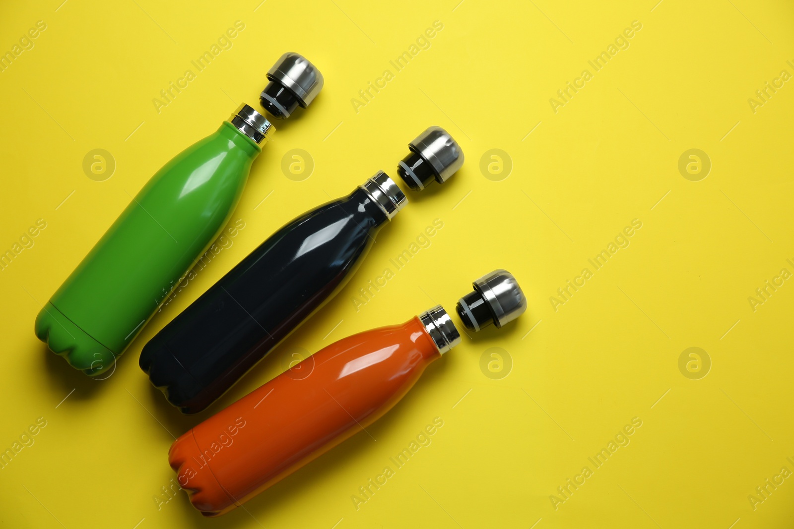 Photo of Different thermo bottles on yellow background, flat lay