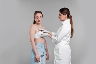 Mammologist checking woman's breast on gray background