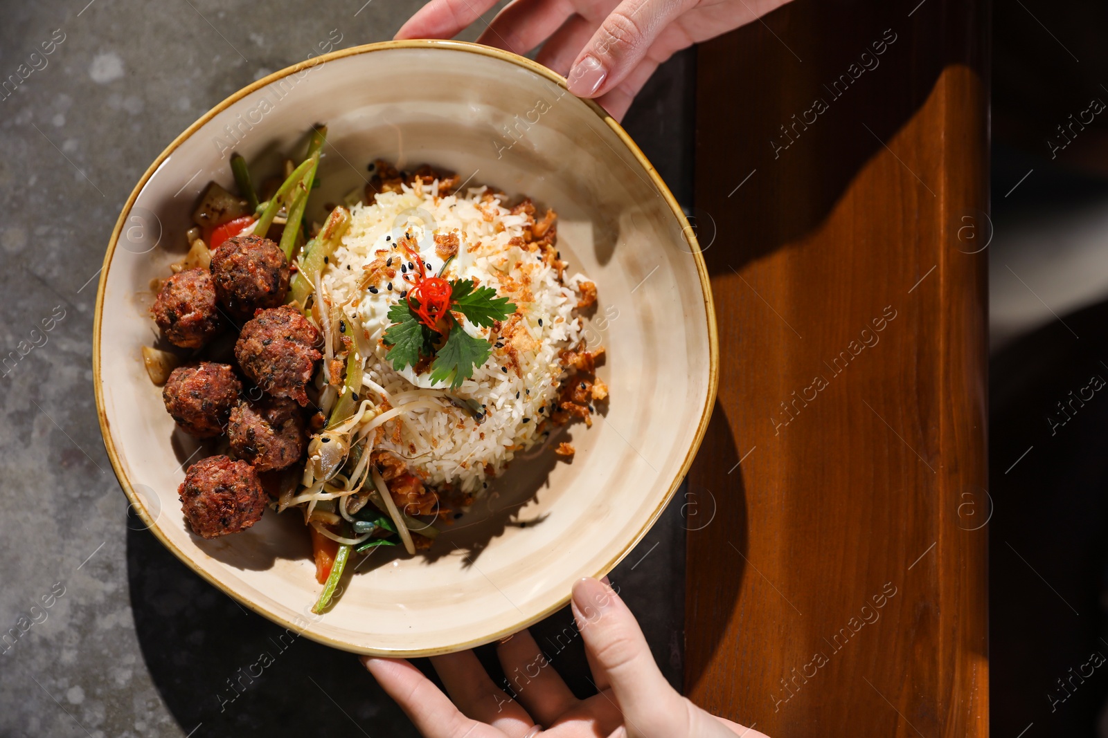 Photo of Woman with plate of rice and meat balls at table, top view