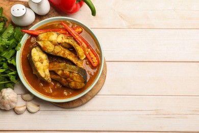 Photo of Tasty fish curry and ingredients on white wooden table, flat lay. Space for text. Indian cuisine