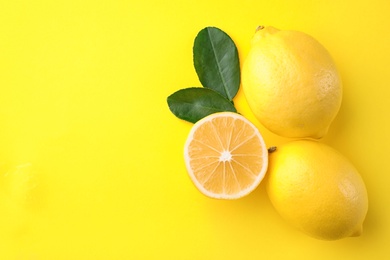 Fresh lemons and leaves on yellow background, flat lay. Space for text