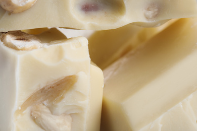 Pieces of tasty white chocolate with nuts as background, closeup