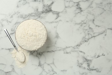 Ceramic bowl with flour on white marble table, flat lay and space for text. Cooking utensils