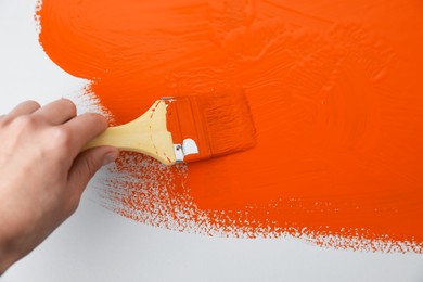Photo of Man applying orange paint with brush on white background, closeup