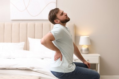 Photo of Man suffering from back pain at home. Bad posture problem