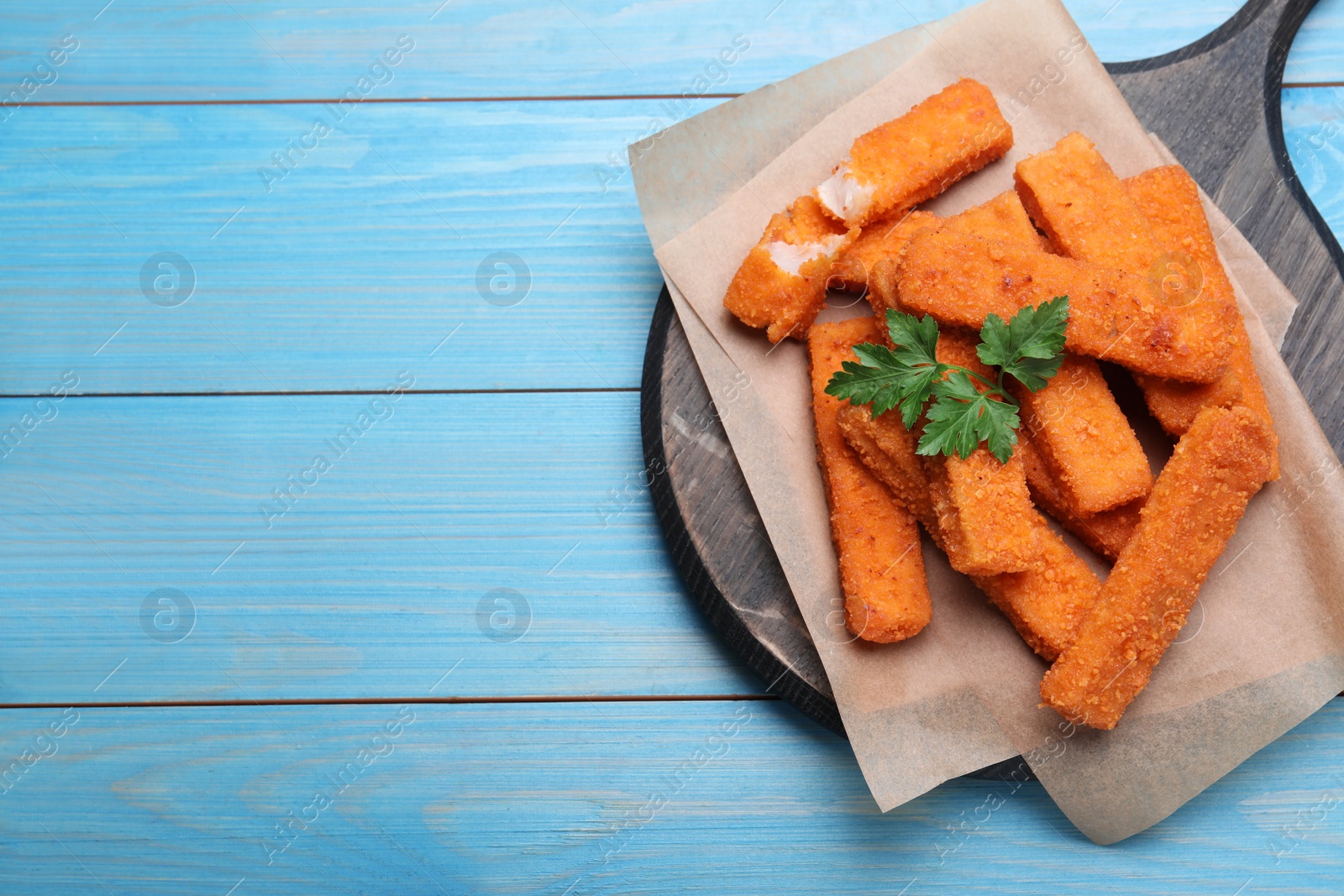 Photo of Fresh breaded fish fingers with parsley served on light blue wooden table, top view. Space for text