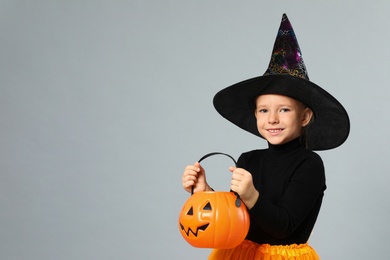 Photo of Cute little girl with pumpkin candy bucket wearing Halloween costume on grey background, space for text