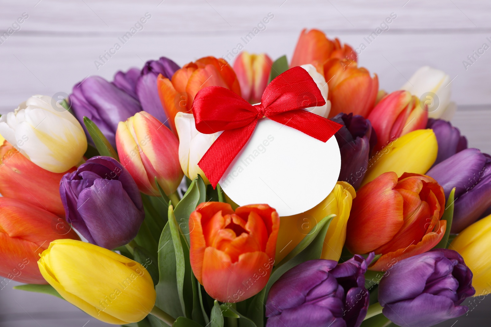 Photo of Bouquet of beautiful colorful tulips with blank card on white wooden background, closeup. Birthday celebration