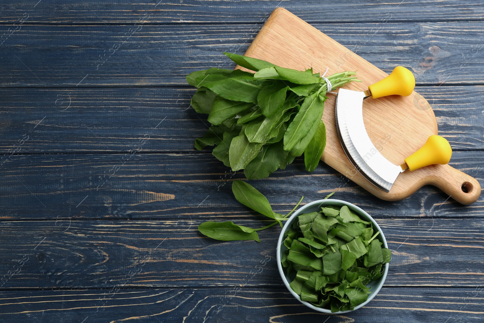 Photo of Fresh green sorrel leaves and mezzaluna knife on blue wooden table, flat lay. Space for text