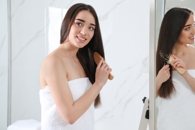 Beautiful young woman with hair brush near mirror in bathroom