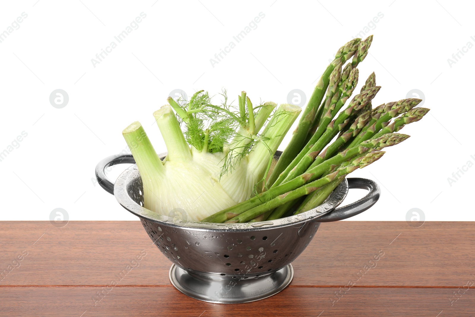 Photo of Metal colander with fennel and asparagus on wooden table against white background