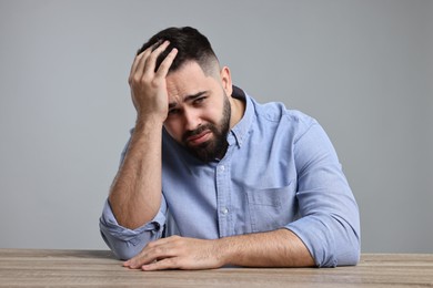 Photo of Portrait of sad man at wooden table on light grey background