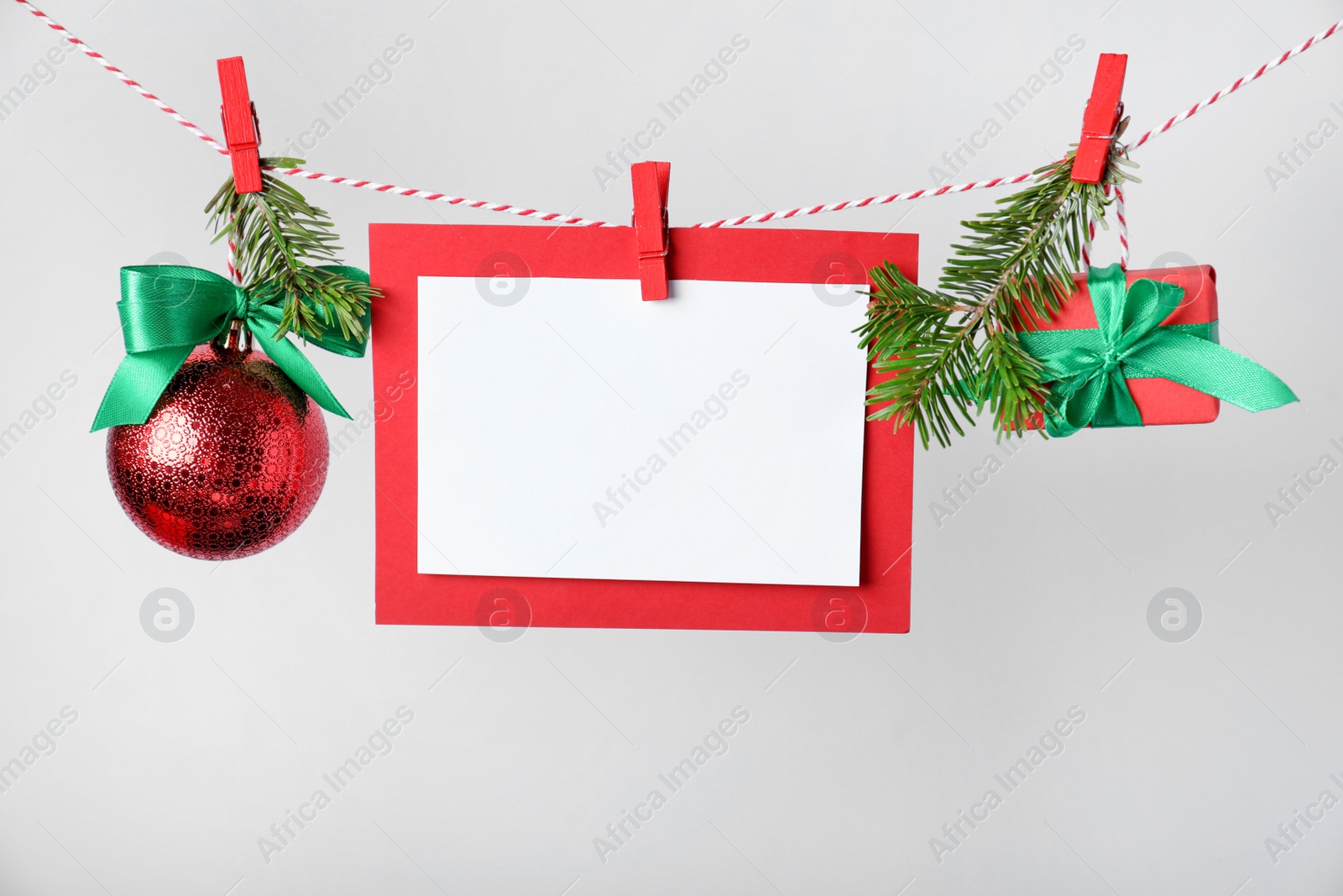 Photo of Blank Christmas card and festive decor on rope against white background, space for text