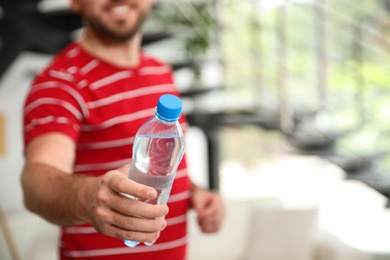 Photo of Young man with bottle of water at home, closeup. Space for text