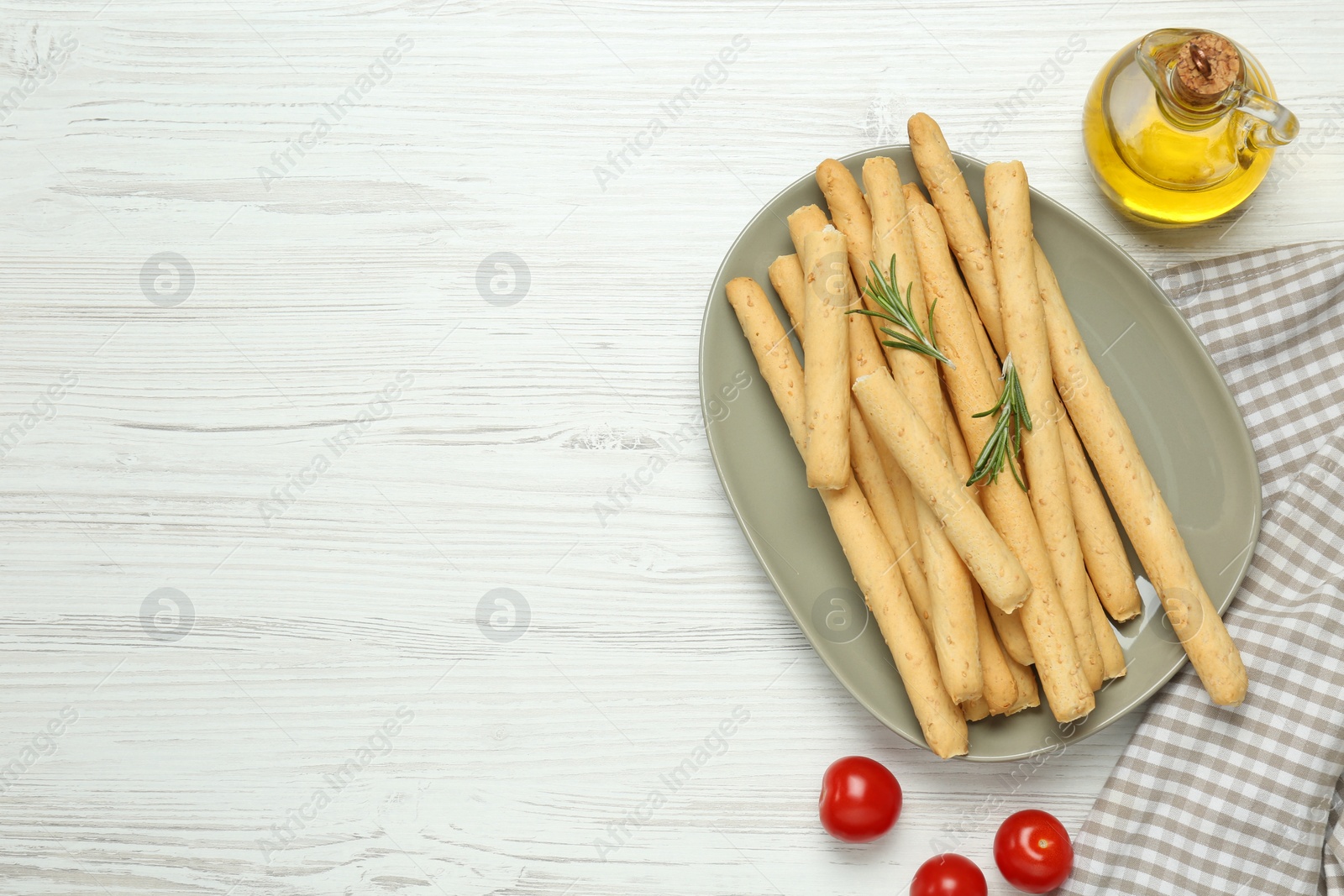 Photo of Delicious grissini, oil, rosemary and tomatoes on white wooden table, flat lay. Space for text