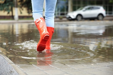 Photo of Woman with red rubber boots in puddle, closeup. Rainy weather