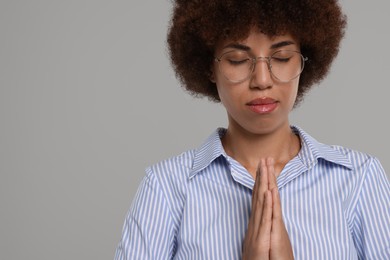 Photo of Woman with clasped hands praying to God on grey background. Space for text